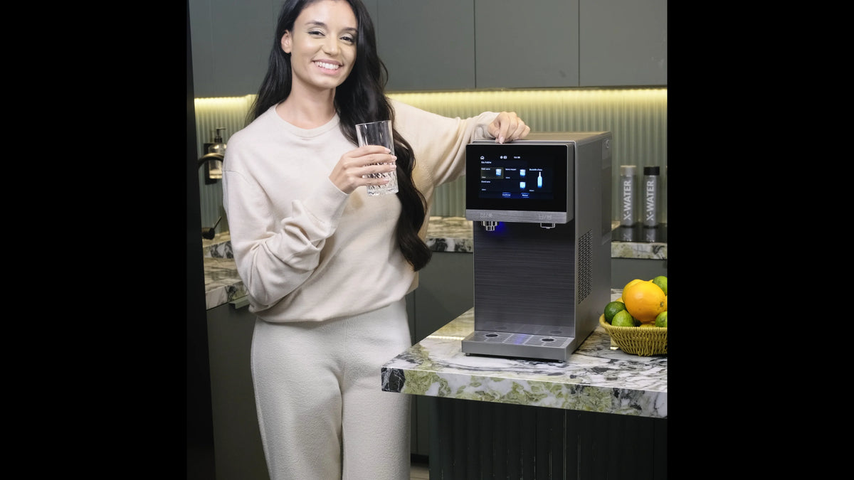 Personne à côté d’un appareil de boisson posé sur un plan de travail, tenant un verre transparent